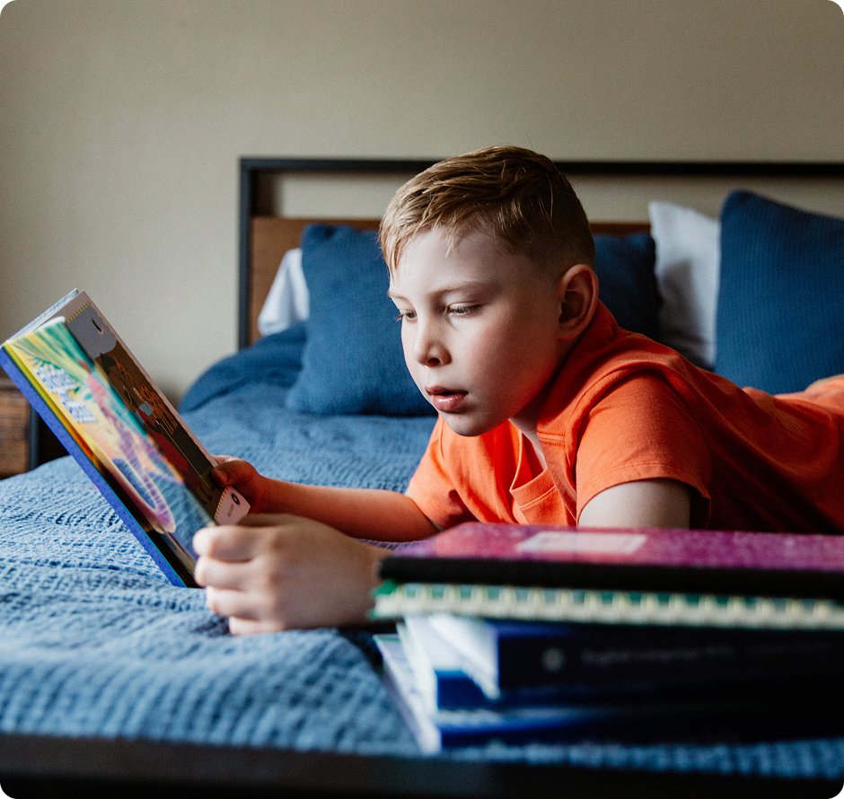 Elementary student reading a book in his bed