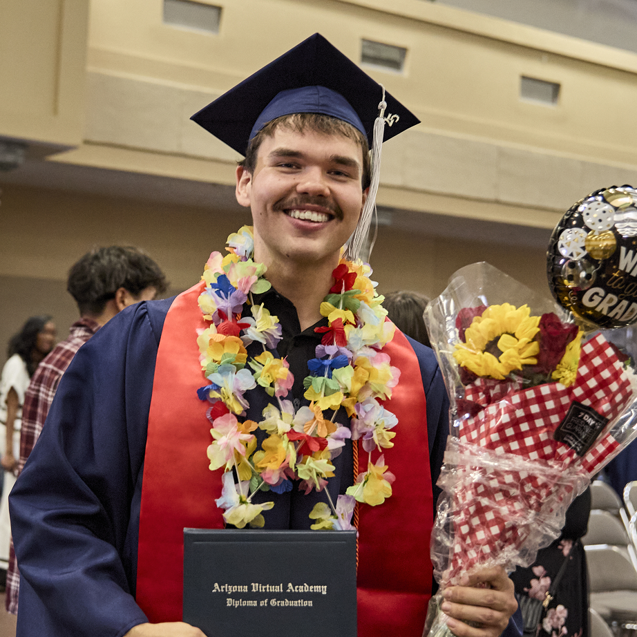 Graduated student smiling at the camera using his graduation hat and holding his diploma